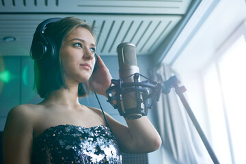 Purposeful professional musician singing son in front of microphone in recording studio