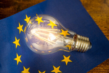 A glowing light bulb lying in the middle of the European Union flag, Concept, Energy prices in EU...