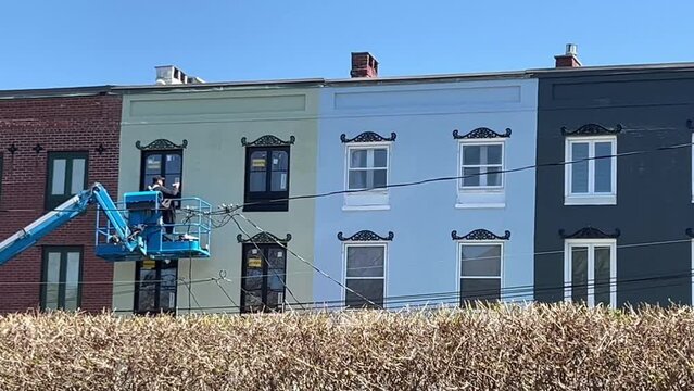 Man Applying Paint to Exterior Trim From Elevated Lift, Colorful Urban Row Houses
