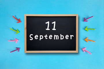 September 11 written in chalk on black board. Calendar date 11th of September on chalkboard on blue...