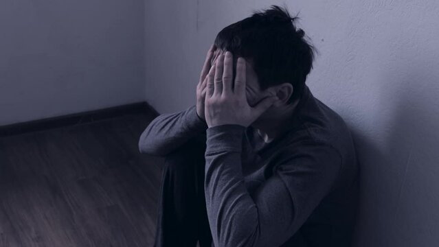 Unhappy unrecognizable man sitting in the corner of the room and holding his head. The concept of psychological, mental and life or family and intimate problems