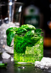 Green summer alcoholic cocktail drink with dry gin, sugar syrup, lemon, green basil and ice, dark...