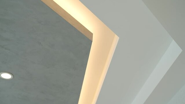 Contemporary interior featuring geometric ceiling design with deep recess illuminated with cozy light. Interplay of light and shadow on textured surface of premium materials in new apartment