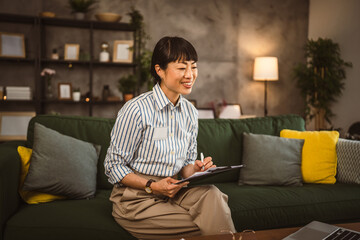 Mature japanese woman hold clipboard and look at laptop work from home