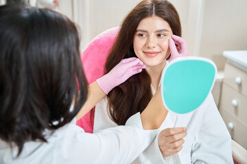Joyous young woman undergoing facial skin examination in beauty clinic - 797055143