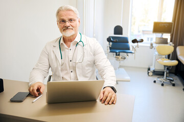 Therapist in white coat sitting at laptop in clinical office