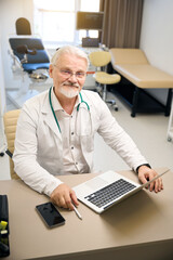 Therapist in white coat sitting at laptop in medical office