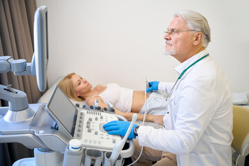 Mature man using ultrasound scan examining female patient in modern hospital - 797062550