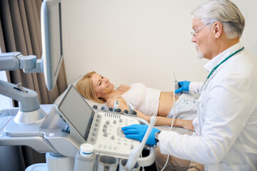 Mature man using ultrasound scan examining woman in modern hospital - 797062910