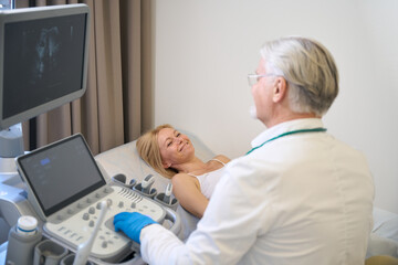 Doctor using ultrasound scan examining smiling woman - 797063762