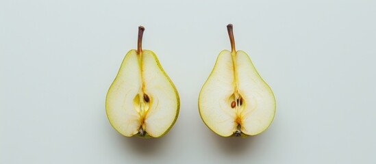 Two green pears sliced in half resting on top of a table with a white surface.