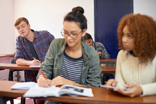 College student, man and copying test in classroom with reading, question paper and answers at campus. Person, cheating and writing exam with women, info and assessment for education at university