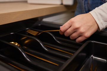 Person grabbing gold fork from black drawer with handles