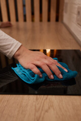 A person is cleaning a black stove top with a blue cloth