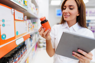 Beautiful pharmacist working and standing in a drug store and doing a stock take. Portrait of a...