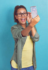 Happy woman, nerd and glasses with selfie for picture, memory or review on a blue studio...