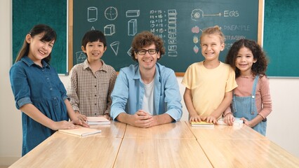 Professional caucasian teacher and diverse student looking at camera while happy school boy smiling. Group of multicultural children smiling while standing in front of classroom. Education. Pedagogy.