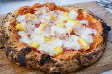 A homemade pizza with pineapple and chicken toppings sits on a wooden cutting board