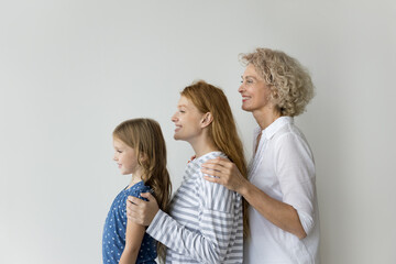 Little girl her young adult mummy and mature grandma posing on gray studio wall background, showing unity, deep-rooted connections, shared history among family members across different stages of life