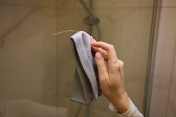 Person using cloth to clean shower door handle in bathroom
