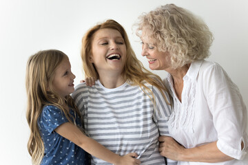 Happy young 30s woman laughing posing on gray studio wall with little 5s daughter and aged 60s mother, family hugging, showing life values, having good strong relationships, feeling unconditional love