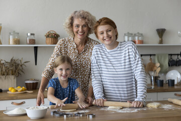 Intergenerational bonding, culinary traditions. Two generations of women and little girl cook, pose for camera, enjoy cookery, warm relations, creating lasting memories and connection through cooking