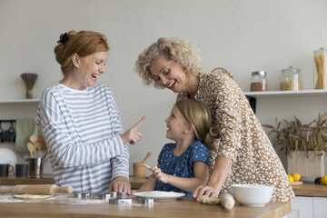 Little 6s girl cooking with loving mom and granny in kitchen, playful multi-generational family...