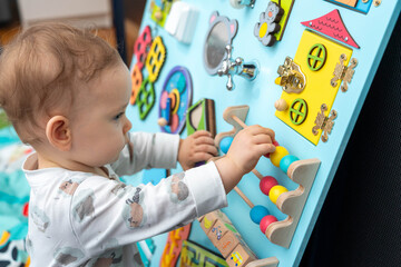 Profile of a cute baby playing with wooden elements on a busy board