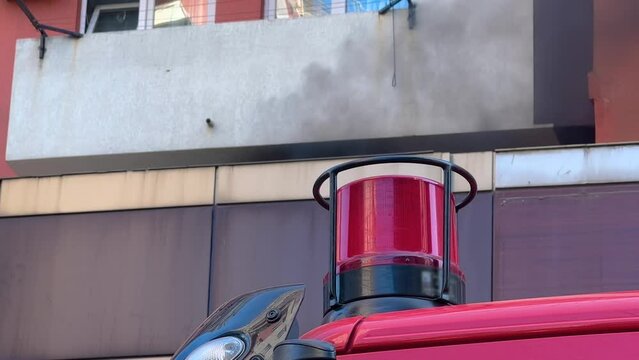 Close up view: red flashing signal light on the fire truck, fire engine. Dark smoke from the fire is pouring out of the window of building. Emergency vehicle lighting, firefighting and alarm concept