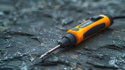 Black and yellow manual screwdriver lying on a textured black surface with visible wear.