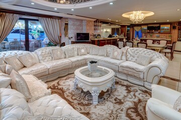 A luxurious Neo-classic living room with ornate white furniture, elegant chandelier, and sophisticated decor, leading to an outdoor area.