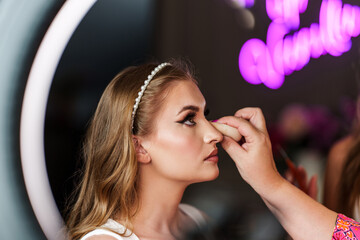 Professional beautician applying makeup on beautiful young woman's face. Professional make up studio work with gorgeous female model.
