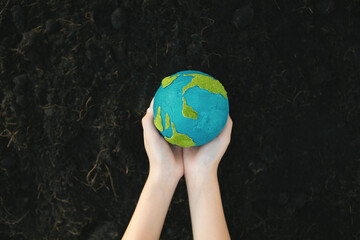 Young boy's hand holding planet Earth globe on fertile soil background as Earth day to save this...