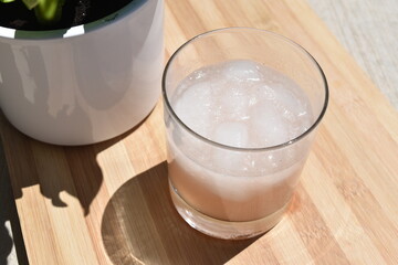 Iced drink on wood cutting board, sunny with plant, close up.