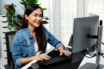 Working young beautiful asian creative manager typing keyboard to search on pc with website design on social media channel online planning with blue jeans shirt at modern home office. Stratagem.
