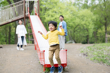 新緑の公園の滑り台で遊ぶアジア人（日本人）の親子...