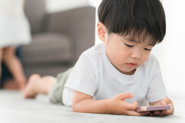 リビングでスマホで動画・ゲームをするアジア人の男の子
