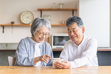 スマホ・スマートフォンのアプリを使うアジア人高齢者夫婦（笑顔・楽しい）
