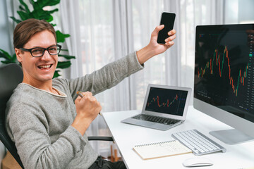 Smart business trader in casual day looking at camera with raising fist up and showing the phone...
