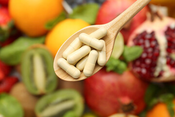 Vitamin pills in spoon over fresh fruits, top view