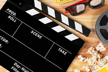 Clapperboard, 3D glasses, popcorn and film reel on wooden table, flat lay