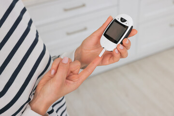 Diabetes. Woman checking blood sugar level with glucometer in kitchen, closeup