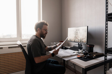A focused photographer analyzes film negatives in a well-lit, modern home office, surrounded by...