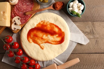 Pizza dough with tomato sauce and products on wooden table, flat lay