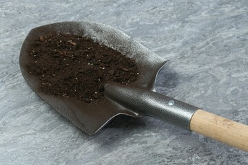 Metal shovel with fertile soil on gray textured surface, closeup