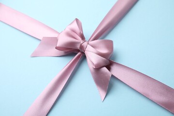 Pink satin ribbon with bow on light blue background, closeup