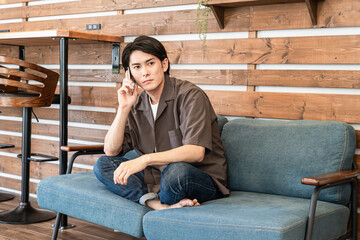 自宅のソファに座りスマホで通話する若いアジア人男性
