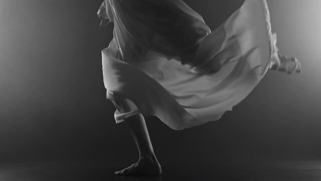 Ballet dancer legs jumping barefoot on stage. Woman practices exercises. Ballerina feet. Unrecognizable professional lady shows classic pas in silk dress