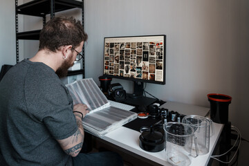 A focused photographer examining film negatives in a well-equipped, contemporary workspace filled with photography equipment.