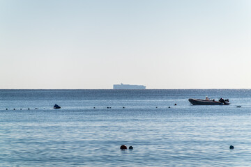 Calm blue sea with the silhouette of a large ship on the horizon